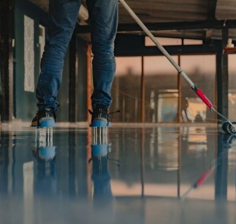 Technician in spiked shoes applies smooth epoxy coating in a commercial space in Aurora.