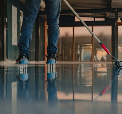 Worker applying epoxy floor coating in Barrie using spiked shoes and a roller applicator.