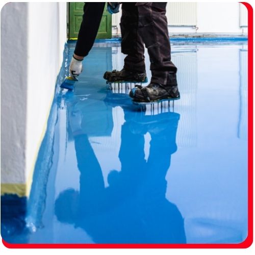 Worker applying blue epoxy coating in Barrie with spiked shoes for even resin distribution.