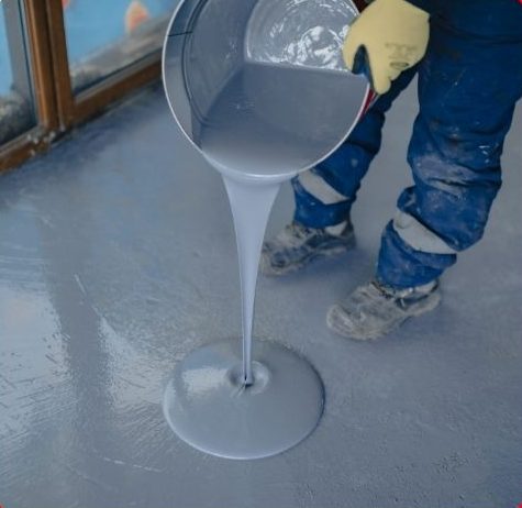 Worker pouring grey epoxy resin onto a concrete floor in Hamilton for commercial flooring installation.