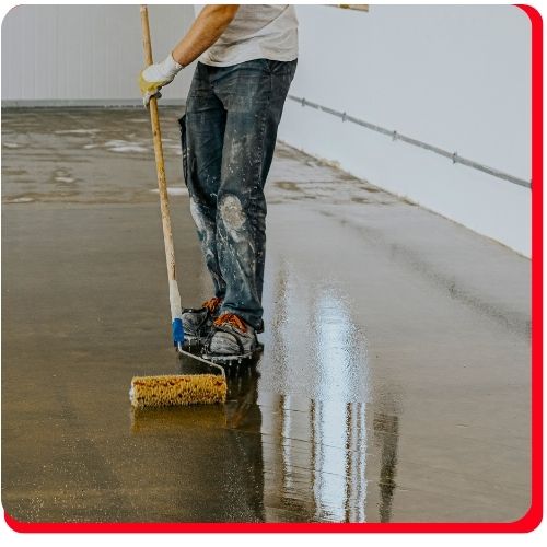 Worker in Hamilton applies epoxy coating to a concrete floor using a roller tool.