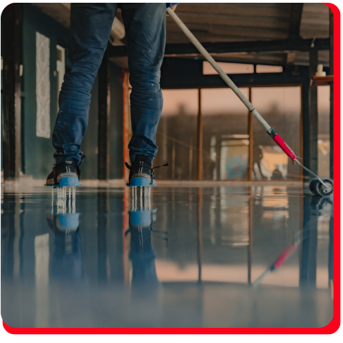 Worker wearing spike shoes applies blue epoxy flooring with a roller in a Markham commercial building.