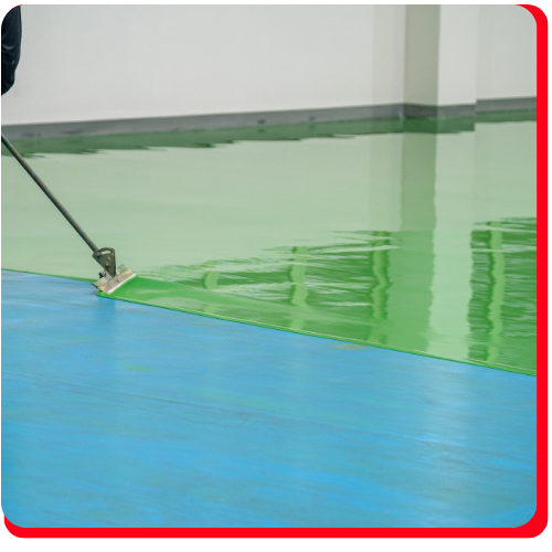 A worker applies vibrant green epoxy over blue flooring in a Markham industrial space.
