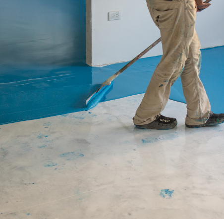 Worker applying blue epoxy coating to a prepared concrete floor in Muskoka.