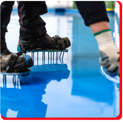 Workers with spiked shoes walking over wet blue epoxy flooring in Richmond Hill.