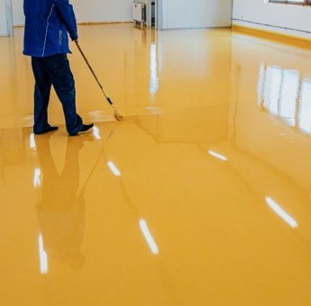 Technician applying a vibrant yellow epoxy coating on a glossy commercial floor in Toronto.