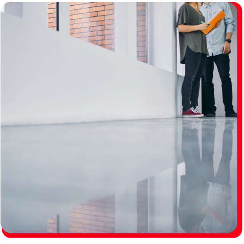 Two people standing on a smooth, light-grey waterproof epoxy floor inside an organized industrial warehouse in Hamilton.